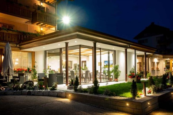 Prosklená restaurace osvětlená v noci s moderním vybavením a květinovou výzdobou.