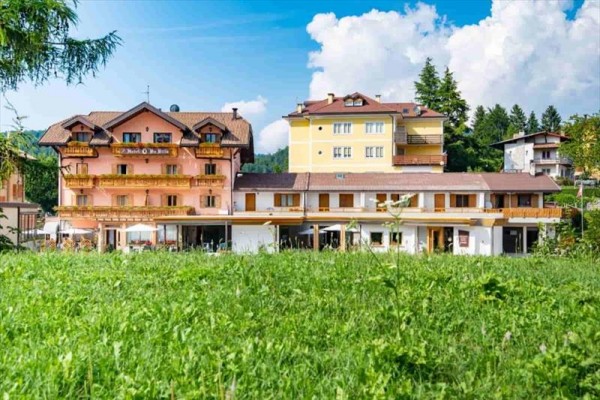 Barevný hotel s více patry, obklopený zelení a modrou oblohou.