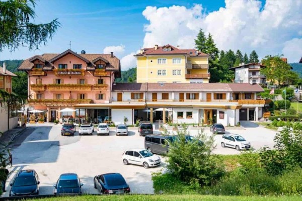 Budovy s parkovištěm plným aut a zelenými stromy v pozadí.