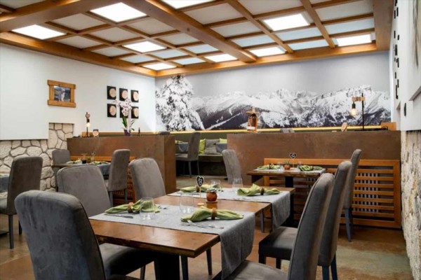 Interiér restaurace s dekoracemi ve stylu dřeva a kámen, na stěně velká černobílá fotografie hor.