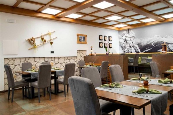 Restaurace s dřevěným podhledem a dekoracemi na stěnách, stoly s šedými ubrusy a zelenými ubrousky.