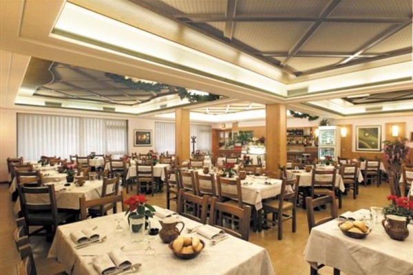 Prostorná restaurace s bílými ubrusy a dřevěnými stoly.