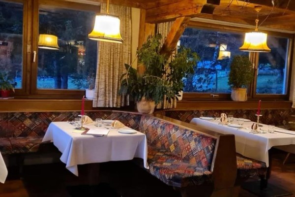 Restaurace s dřevěnými lavicemi a prostřenými stoly u okna s výhledem do přírody.  