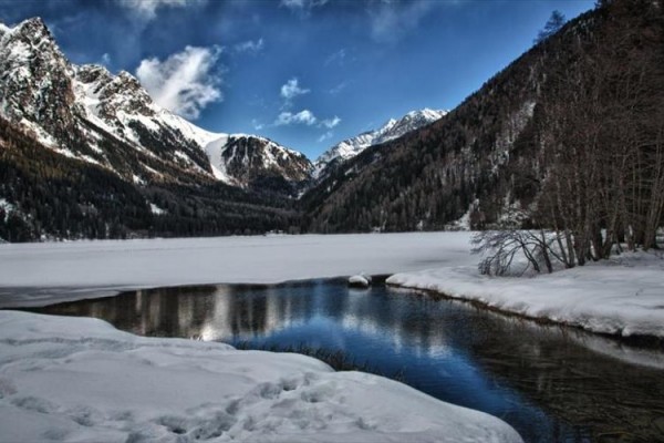 Zamrzlé jezero obklopené zasněženými horami pod modrou oblohou.