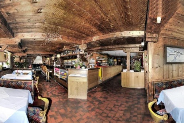 Restaurace s dřevěnými stropy a nábytkem, prostřené stoly a bar v pozadí.