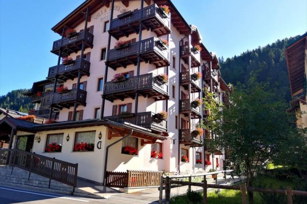 Vícepodlažní hotel s dřevěnými balkóny a květinami v malebné horské oblasti.