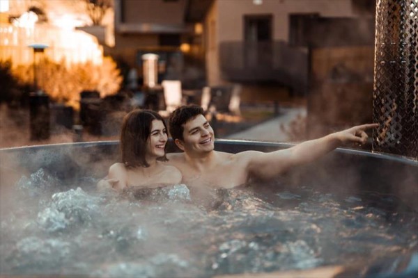 Dva lidé se smějí a relaxují ve venkovní vířivce obklopeni párou.