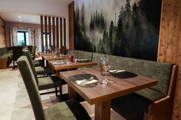 Restaurace s dřevěným nábytkem a nástěnnou malbou lesa.