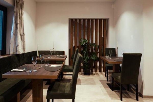Restaurace s dřevěnými stoly, jednoduchým nábytkem a rostlinou v rohu.