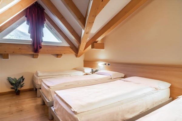 Podkrovní pokoj se třemi jednolůžkovými postelemi a šikmým stropem s dřevěnými trámy.
