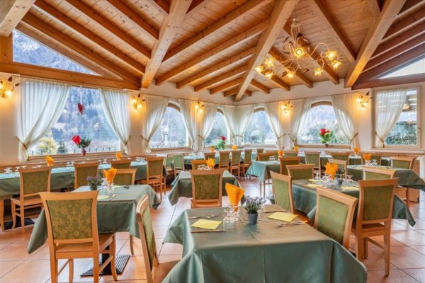 Světlá restaurace s dřevěným stropem, zelenými ubrusy a velkými okny s výhledem na hory.