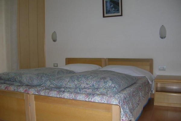 Dřevěná manželská postel s nočním stolkem v ložnici.