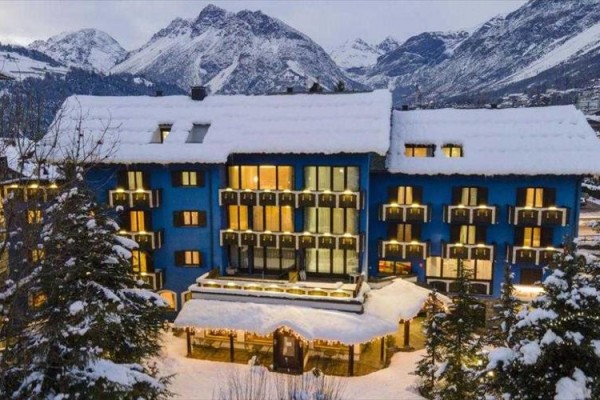 Modrá budova hotelu pokrytá sněhem v zasněžených horách.