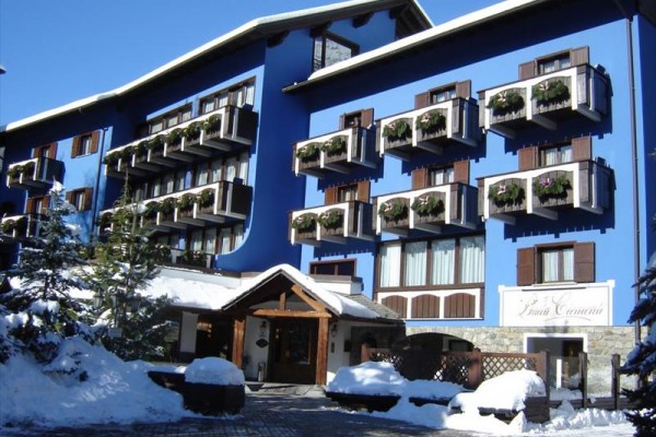 Modrá budova hotelu se zasněženým okolím a balkony s rostlinami.