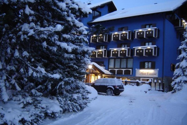 Modrá budova hotelu pokrytá sněhem v zasněžených horách.