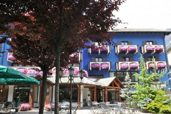 Modrý hotel obklopený zasněženými horami a stromy.
