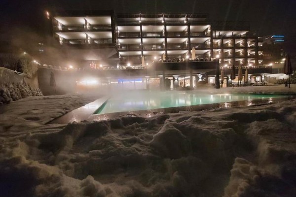 Osvětlený hotel s vyhřívaným bazénem a sněhem v popředí za tmavé noci.  
