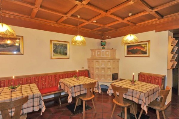 Interiér restaurace s dřevěným obložením, čtyřmi stoly se kostkovanými ubrusy a kachlovými kamny.