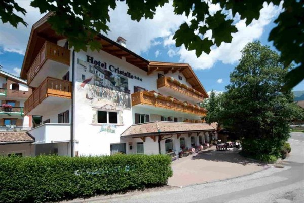 Budova hotelu Cristallo s balkonem a terasou, obklopená zelení.