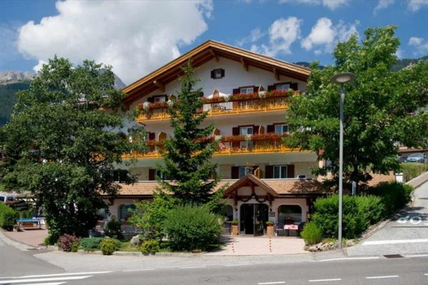 Horský hotel s dřevěnými balkóny obklopený zelení.
