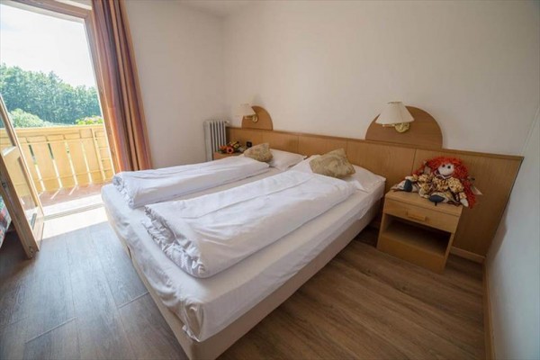 Pokoj s manželskou postelí, nočním stolkem a otevřenými dveřmi na balkón.