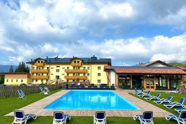 Žlutá budova hotelu se zahradou a venkovním bazénem obklopeným lehátky.