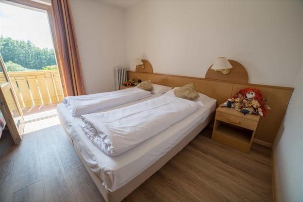 Ložnice s dvojlůžkem a otevřenými dveřmi na balkon.