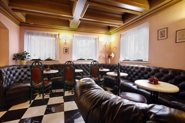 Stylová kavárna s koženými sedačkami, kulatými stoly a židlemi na černobílé šachovnicové podlaze.