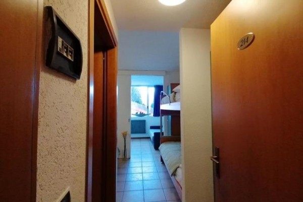 Úzká chodba hotelového pokoje s palandami a otevřenými dveřmi.