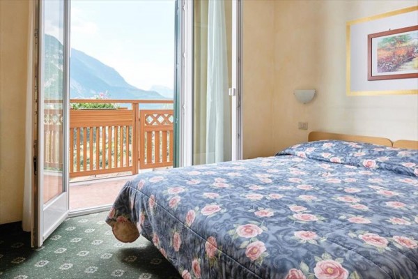 Pokoj s postelí a francouzským oknem vedoucím na balkon s výhledem na hory.