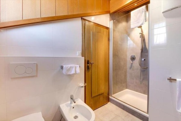 Koupelna s bílými obklady, sprchovým koutem a bidetem.