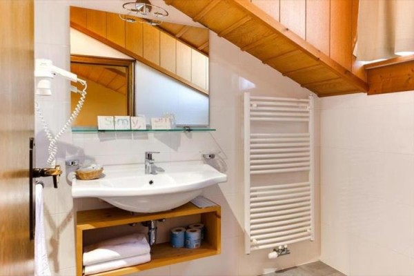 Koupelna se šikmým stropem, umyvadlem, zrcadlem a topným žebříkem.