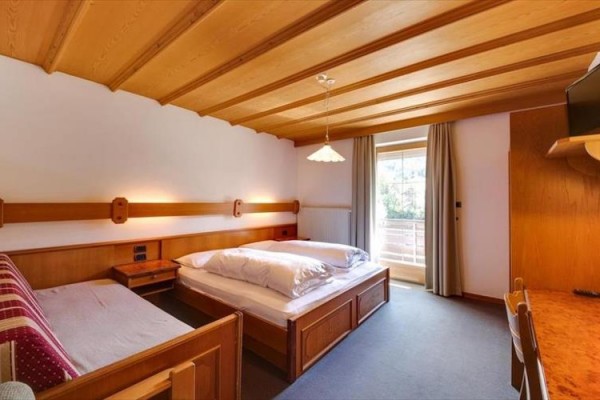 Hotelový pokoj s dřevěným stropem, manželskou postelí, pohovkou a balkónovými dveřmi.