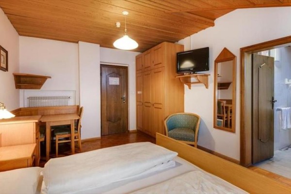 Pokoj s dřevěným nábytkem, televizí, postelí a dveřmi vedoucími do koupelny.