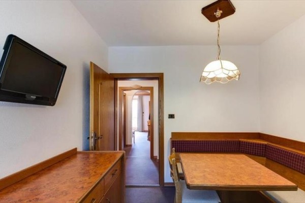 Kuchyňský kout s rohovou lavicí, stolem a televizí na zdi.