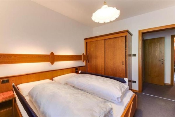 Ložnice s manželskou postelí, dřevěnou skříní a dveřmi.