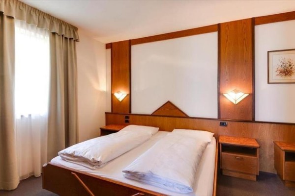 Prostorná ložnice s dvojlůžkem, dřevěným obložením a dvěma nočními stolky.