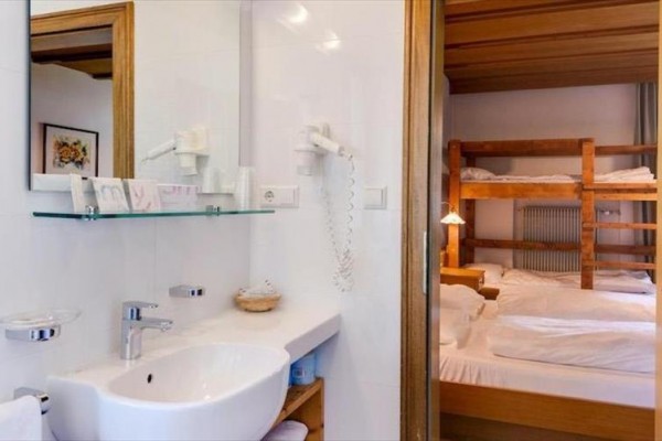 Koupelna s umyvadlem a zrcadlem vedle pokoje s palandou a postelí.