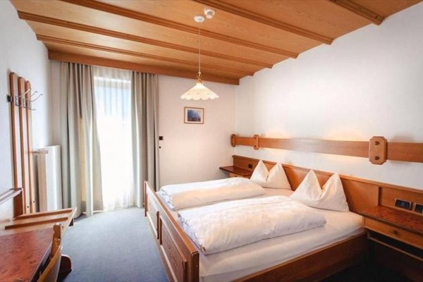 Ložnice s dřevěným nábytkem, manželskou postelí a oknem s bílými závěsy.