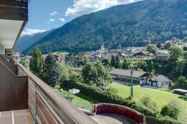 Výhled z balkónu na horskou krajinu s vesnicí v údolí.