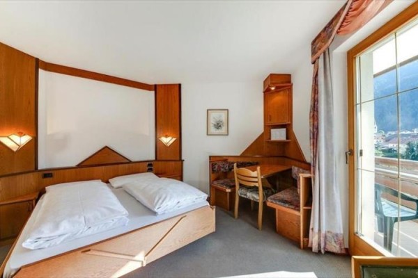 Světlý hotelový pokoj s manželskou postelí, psacím stolem a přístupem na balkon.