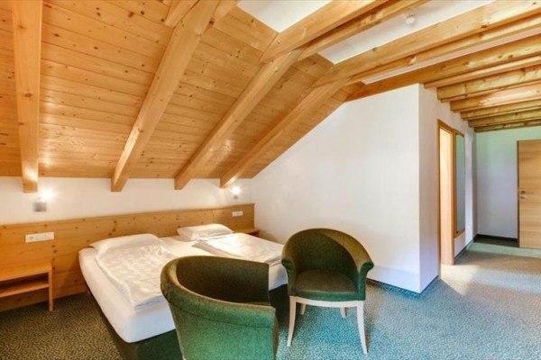 Podkrovní pokoj s manželskou postelí a dvěma zelenými křesly.