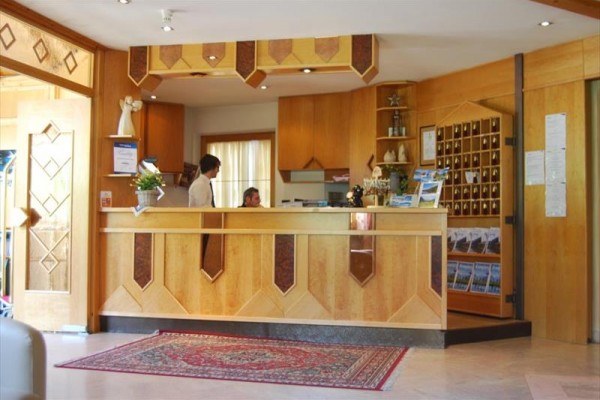 Recepci hotelu s dřevěným pultem obsluhují dva lidé.