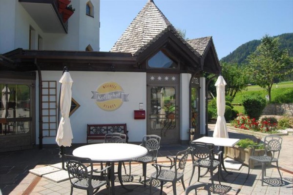 Exteriér kávárny s venkovním posezením a horami v pozadí.