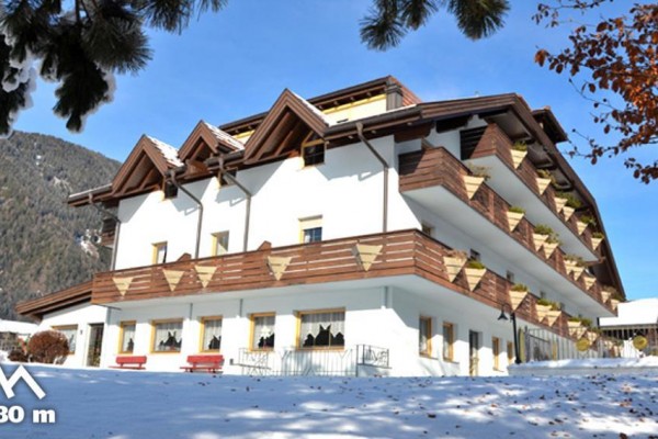 Budova hotelu obklopená sněhem s horskou scenérií v pozadí a nadmořskou výškou 1080 metrů.