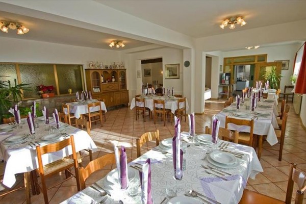 Jídelna s nazdobenými stoly, světle fialové svíčky, a dřevěnými židlemi.