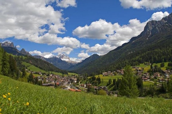 Vesnice v údolí mezi horami s modrou oblohou a mraky.  