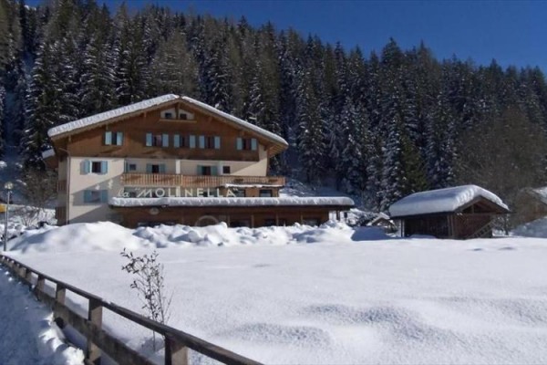 Horská chata obklopená zasněženým lesem za slunečného zimního dne.