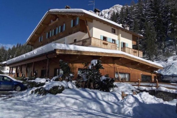 Dřevěná horská chata pokrytá sněhem obklopená stromy.