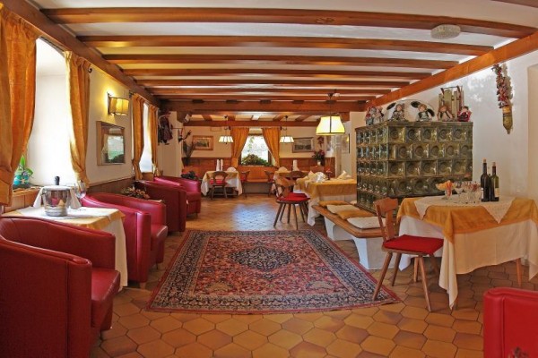 Interiér restaurace s dřevěnými stropy, červenými křesly a perským kobercem.